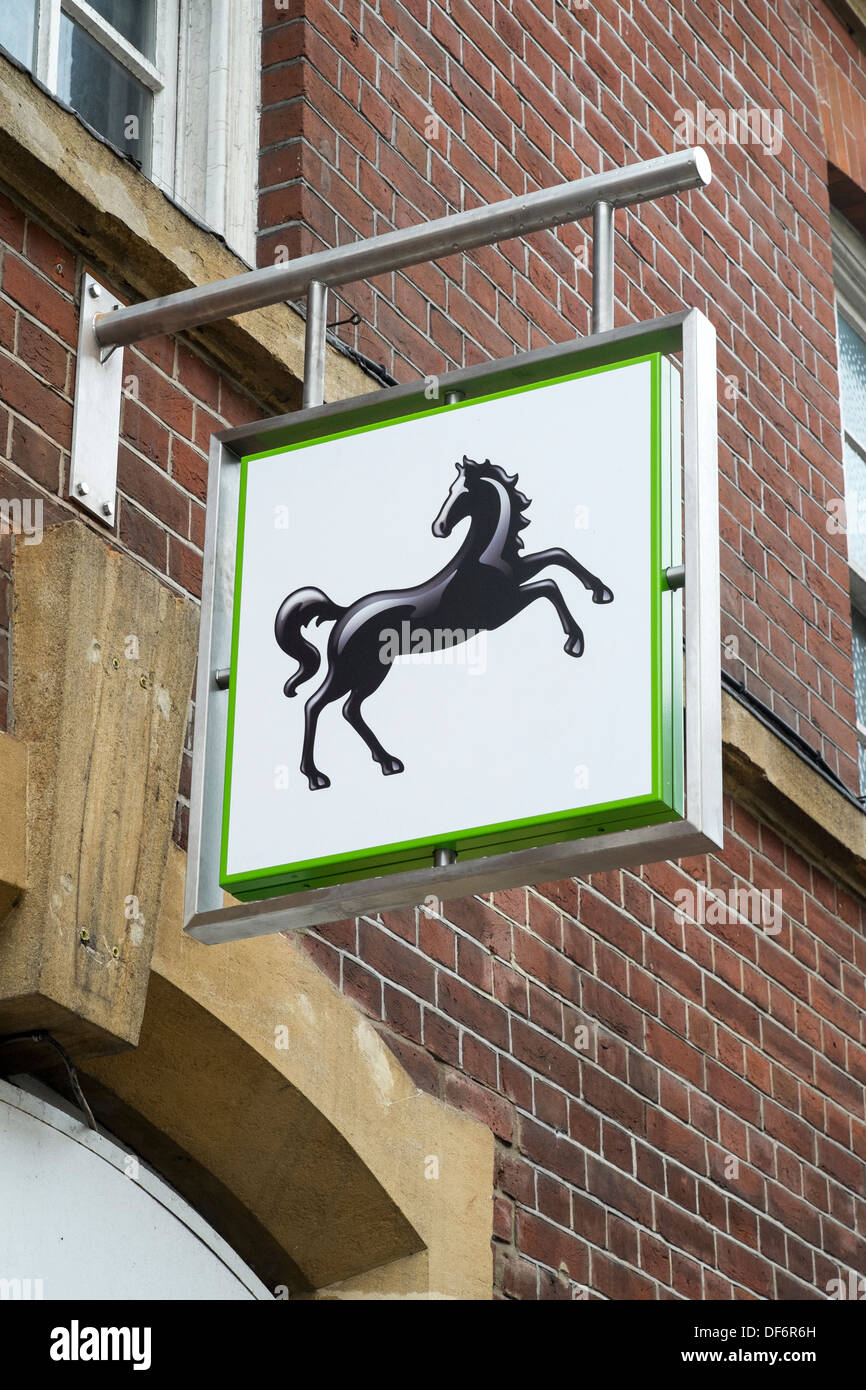 Blickte zu Lloyds Bank schwarzes Pferd Zeichen und Logos oben UK High Street mit Mauer im Hintergrund Stockfoto
