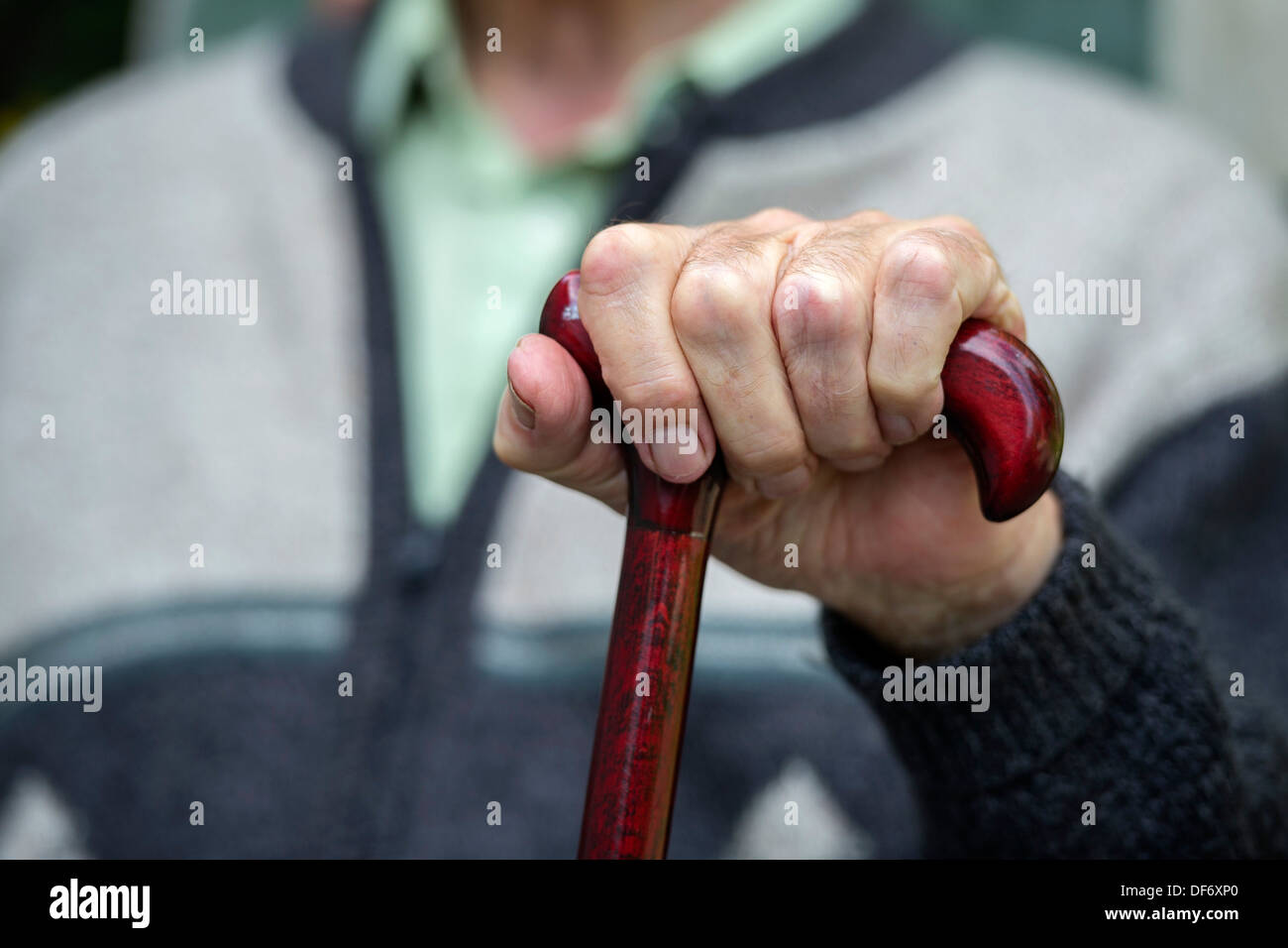 Eine ältere Rentner sitzt mit seinen Händen auf einen Spazierstock in einem Pflegeheim. Stockfoto