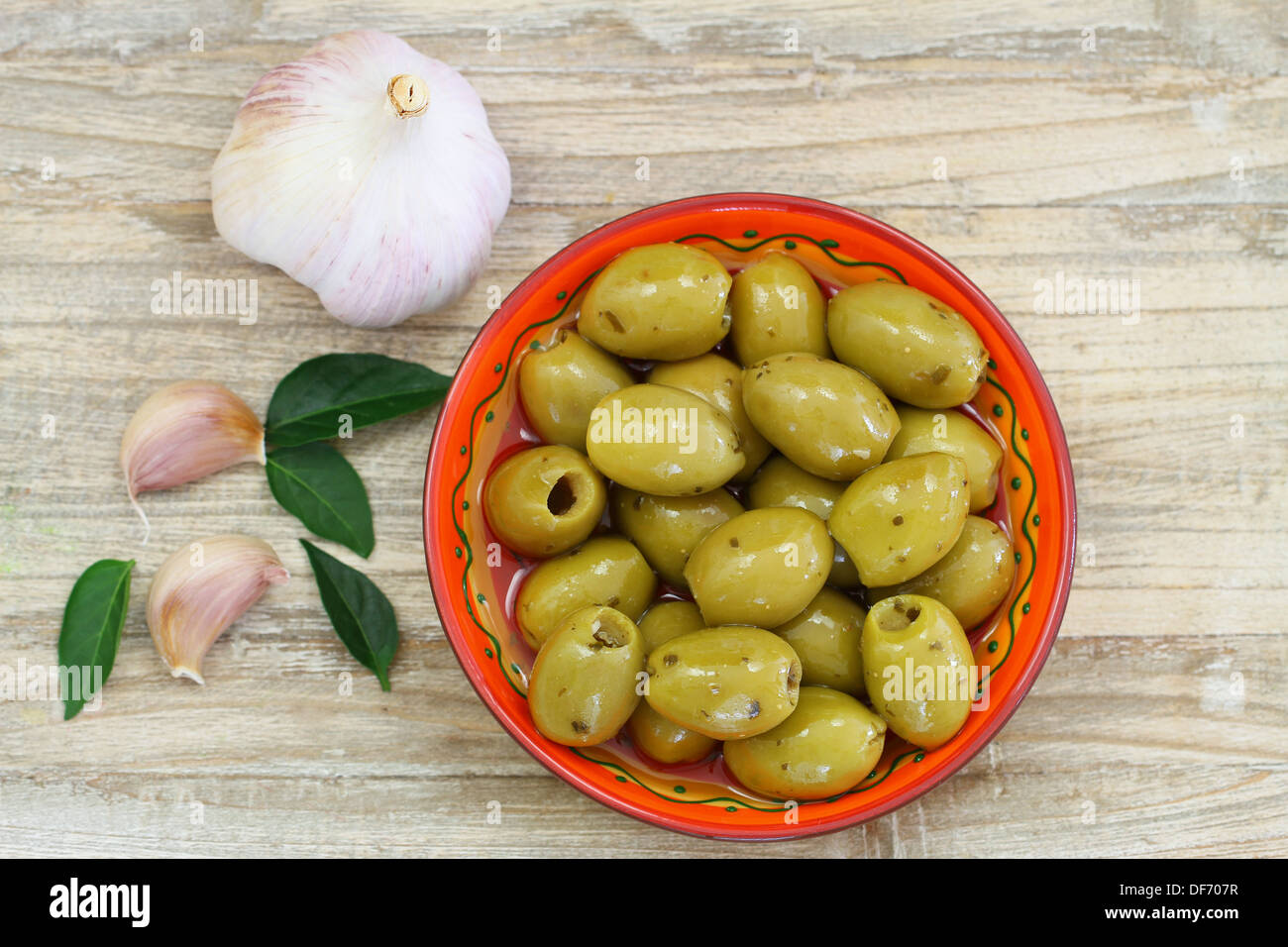 Grüne Oliven mit Knoblauch auf Holzuntergrund Stockfoto