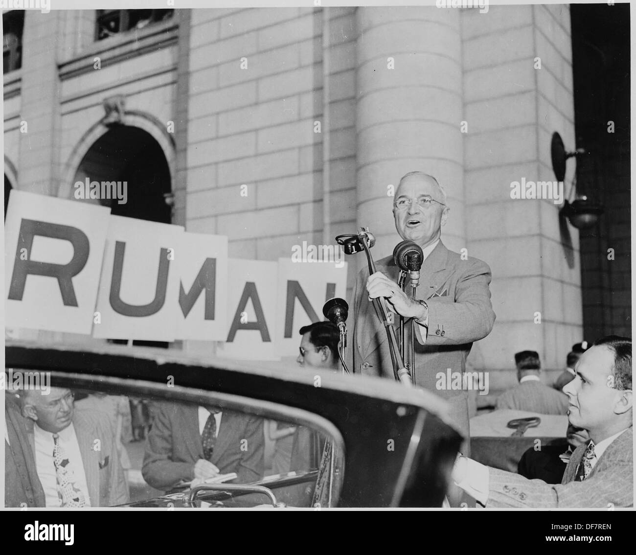 Dieses Bild zeigt Präsident Harry S. Truman, der in einem offenen Auto steht und in ein Mikrofon in Washington, D.C. spricht. Das Foto zeigt einen Moment der öffentlichen Rede oder des politischen Engagements während seiner Präsidentschaft. Stockfoto