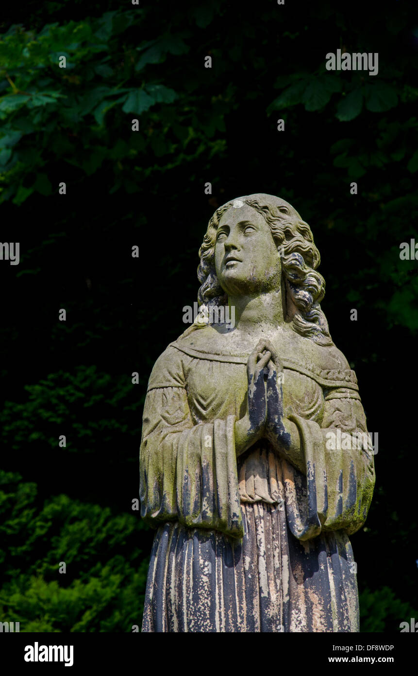 Viktorianische Statue einer Frau mit ihre Hände im Gebet vor dem Hintergrund der Bäume auf dem Friedhof von Dean, Edinburgh. Stockfoto