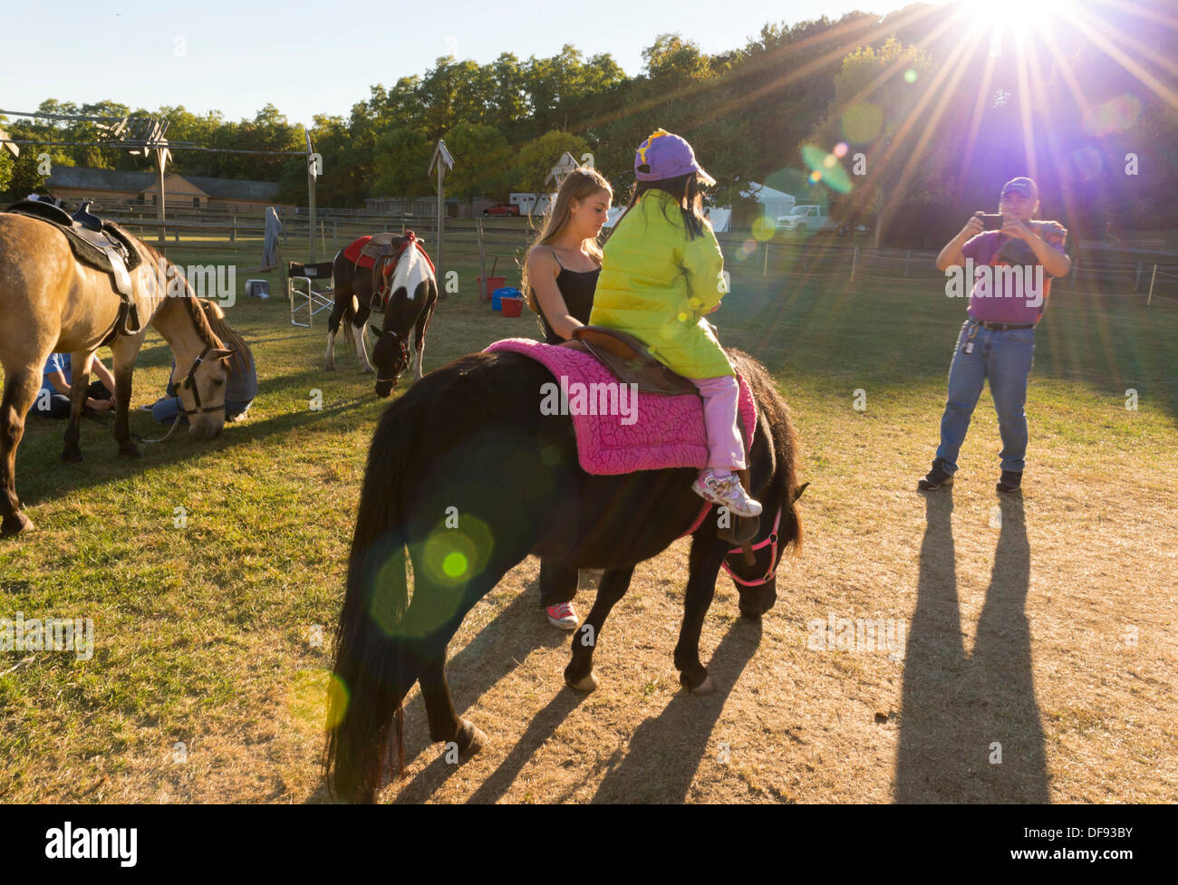 Alten Bethpage, New York, USA 29. September 2013. Ein Vater nimmt ein Foto seiner Tochter ein Pony reiten, als The Long Island Fair Feierabend kommt. Eine jährliche Veranstaltung seit 1842, findet die Kirmes nun an einen rekonstruierten Festplatz am alten Bethpage Village Restaurierung. © Ann E Parry/Alamy-Live-Nachrichten Stockfoto