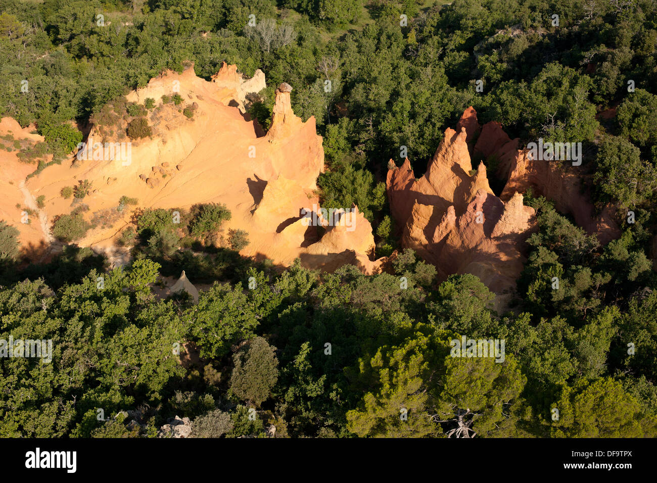 LUFTAUFNAHME. Ockerfarbene Hoodoos in scharfem Kontrast zum umgebenden grünen Laub. Rustrel, Lubéron, Vaucluse, Provence, Frankreich. Stockfoto