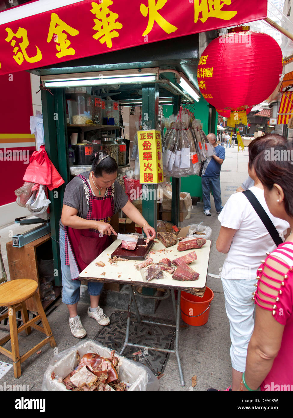 In Sheung Wan Verkaufen getrocknete Wurst und Fisch. Der stall Besitzer ist das Entbeinen einige geheilt Schweinekeule. Stockfoto