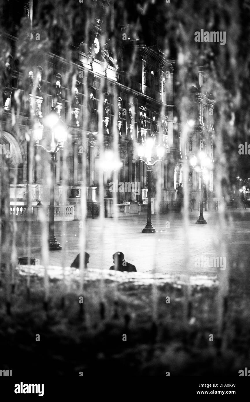 Ein paar sitzen neben dem Brunnen auf der Place de Hôtel de Ville, Paris. Durch die Wasserfontäne fotografiert. Stockfoto