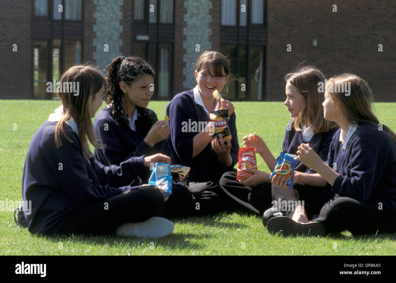 Gruppe von weiterführenden Schulmädchen sitzen auf dem Rasen essen Chips Stockfoto