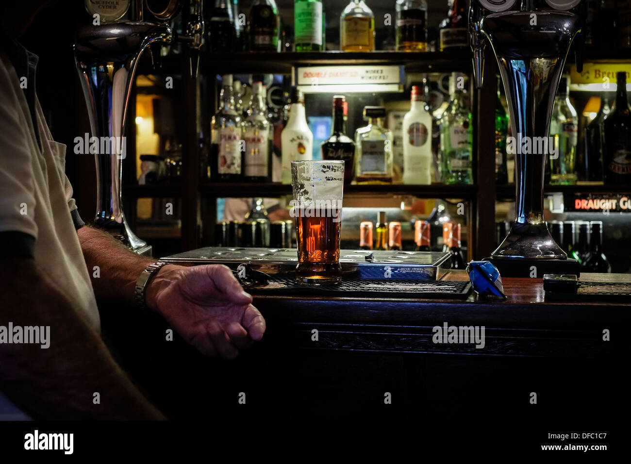 Ein Gast sitzt mit seinem halbleeren Bier an der Bar eines traditionellen Pubs in Großbritannien. Stockfoto