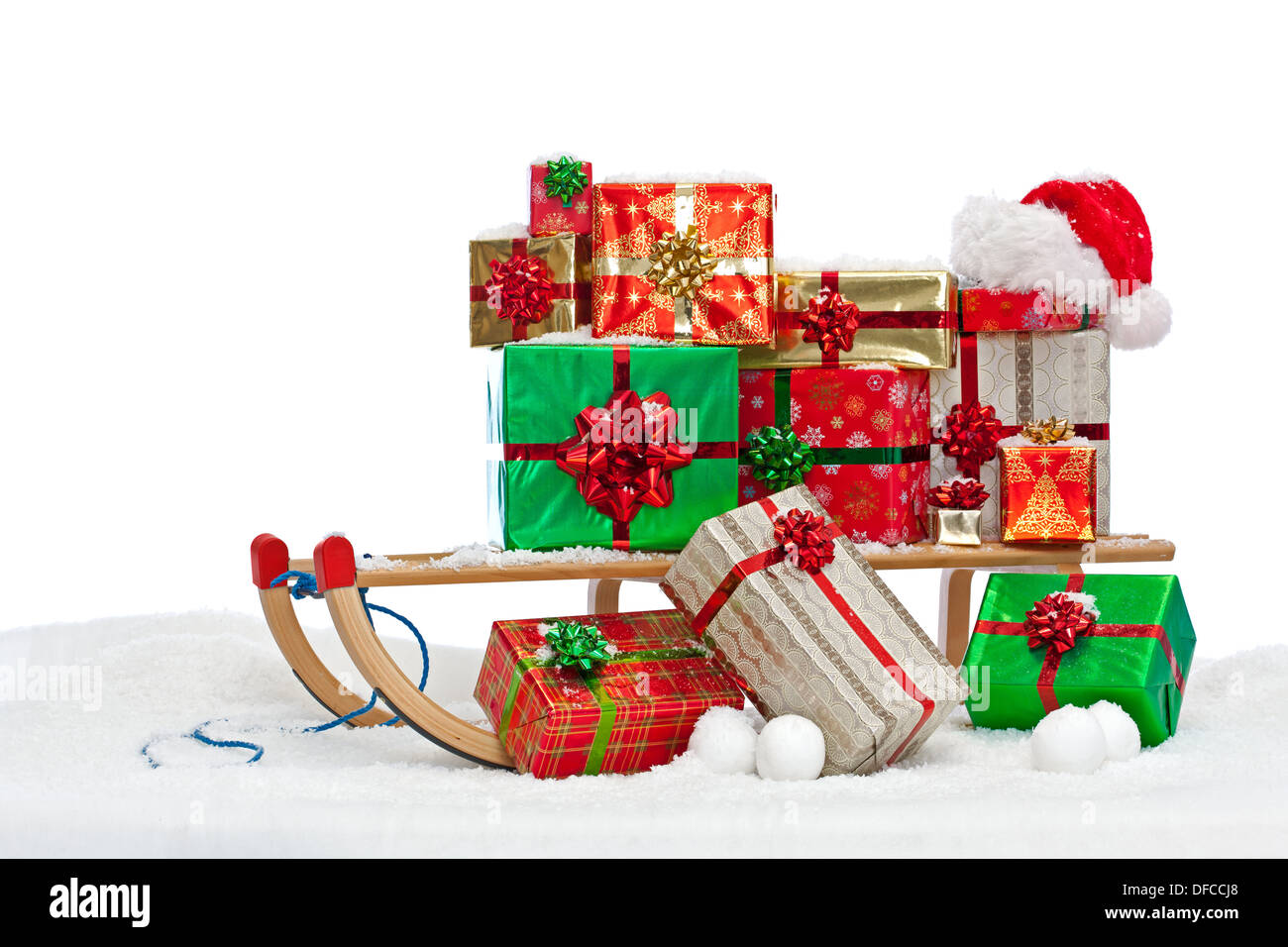 Ein Schlitten beladen mit Geschenk verpackt Weihnachtsgeschenke und eine Weihnachtsmütze, sitzen im Schnee vor einem weißen Hintergrund. Stockfoto