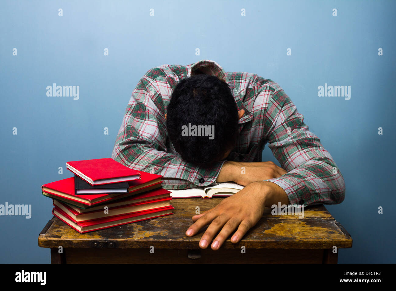 Müder junger Mann schläft auf einem Stapel Bücher Stockfoto