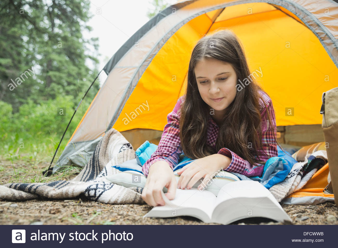 Mädchen lesen Buch beim liegen im Zelt am Campingplatz Stockfoto
