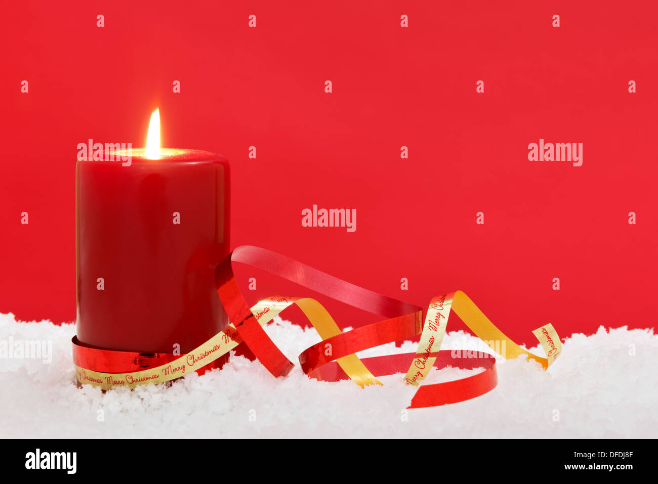 Eine Weihnachtskerze sitzen im Schnee mit Bändern vor einem roten Hintergrund, Ihre eigene festliche Nachricht anzufügen. Stockfoto