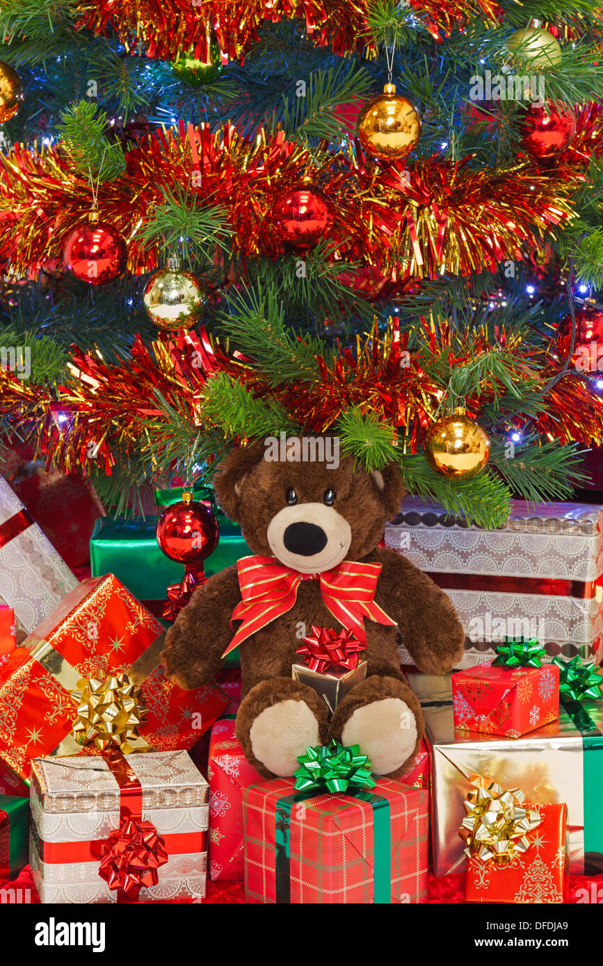 Ein handgemachter Teddybär trägt einen Bogen in unter Geschenke unter dem Weihnachtsbaum. Stockfoto
