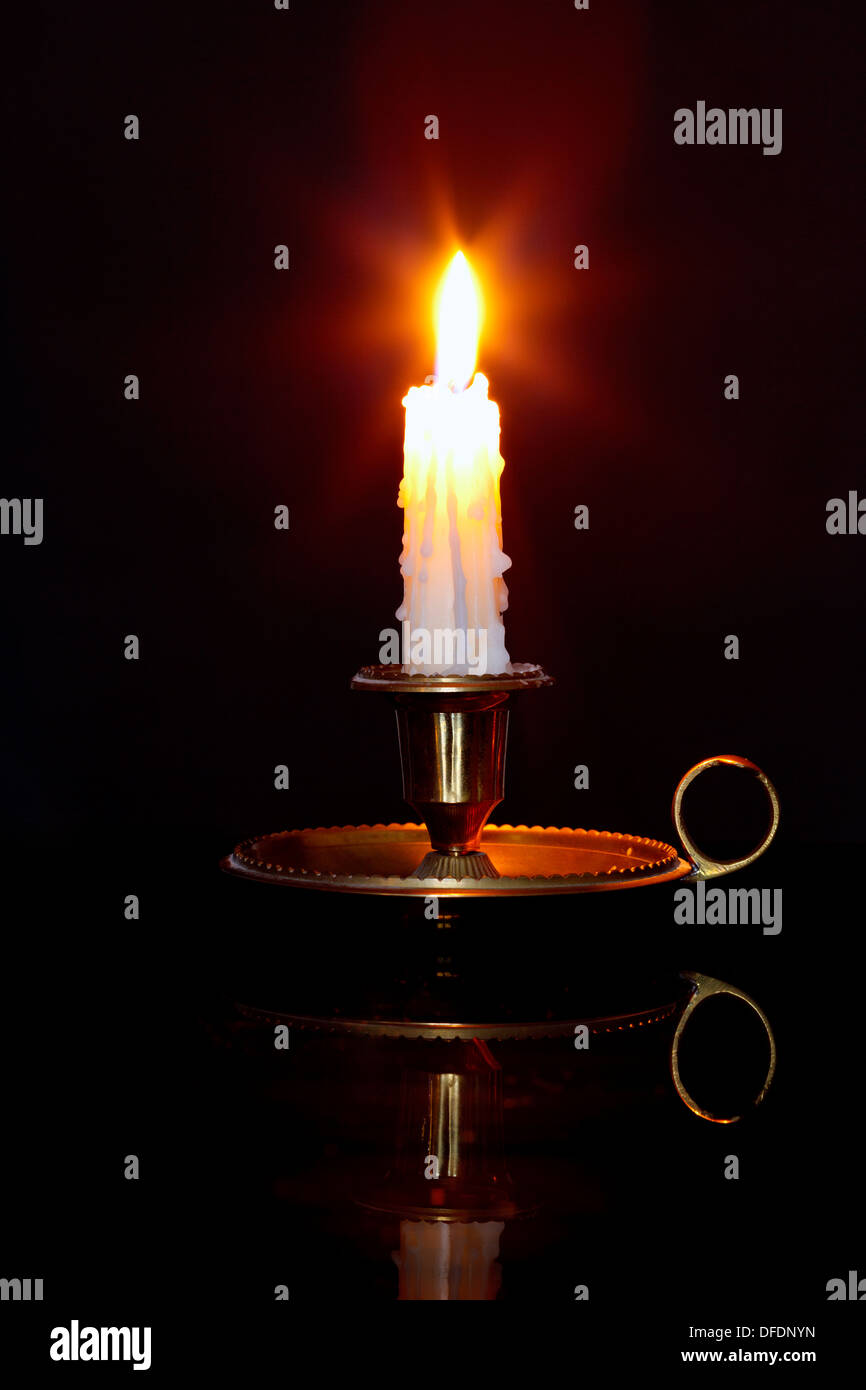 Eine brennende Kerze in einem Messing-Halter, bekannt als ein Chamberstick vor einem schwarzen Hintergrund. Stockfoto