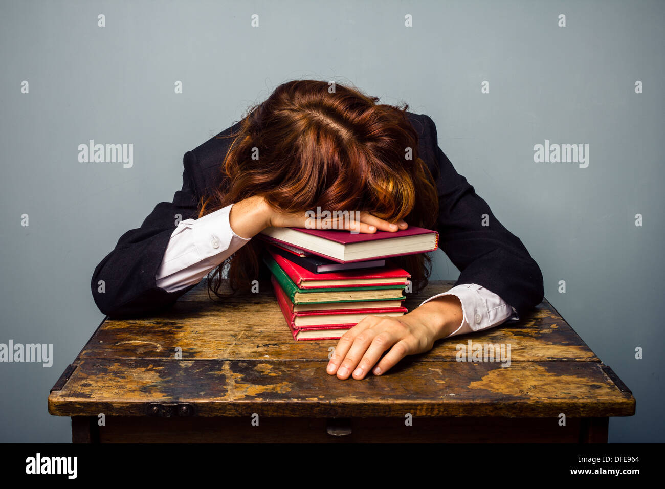 Junge Geschäftsfrau schläft mit dem Kopf ruht auf einem Stapel Bücher vor ihr am Schalter Stockfoto