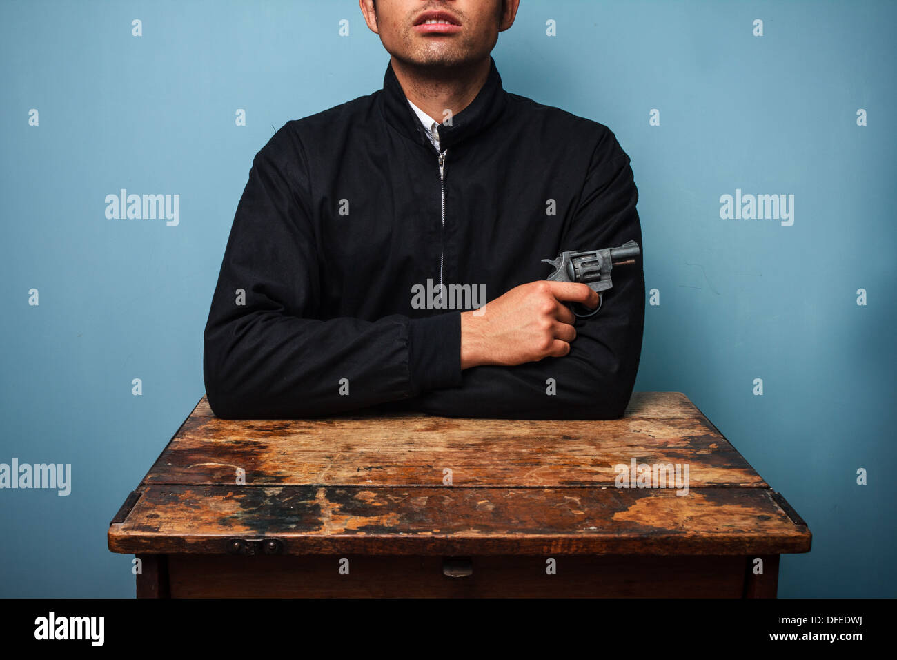 Junger Mann sitzt an einem alten Holztisch mit einer Pistole in der hand Stockfoto