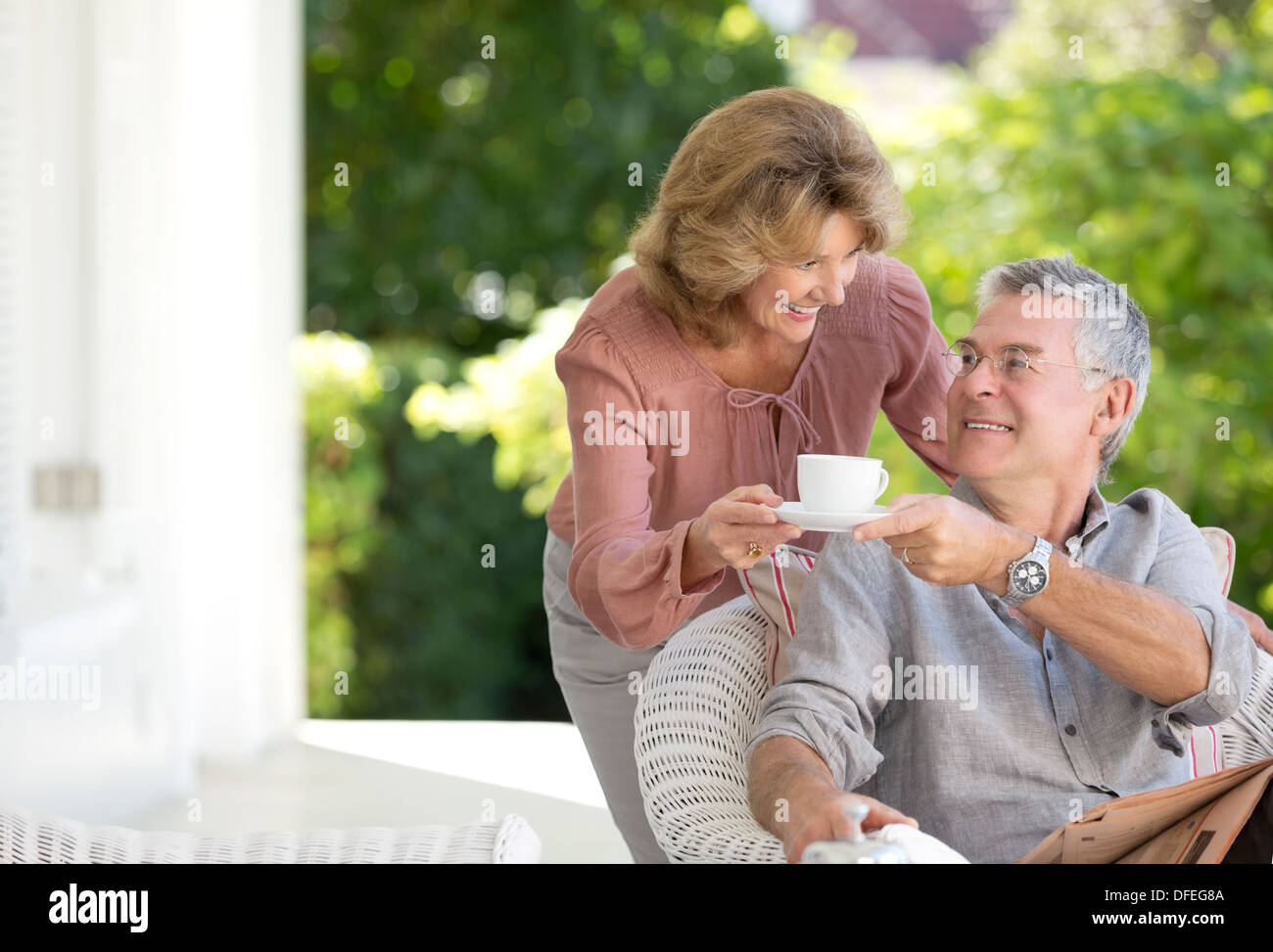 Ältere Frau bringt Mann Tasse Kaffee auf der Terrasse Stockfoto