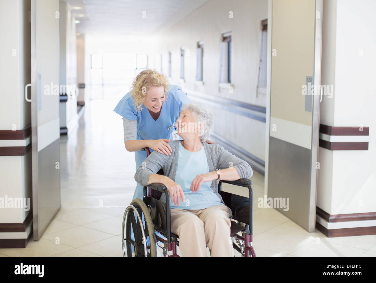Krankenschwester mit alternden Patienten im Rollstuhl im Krankenhausflur Stockfoto