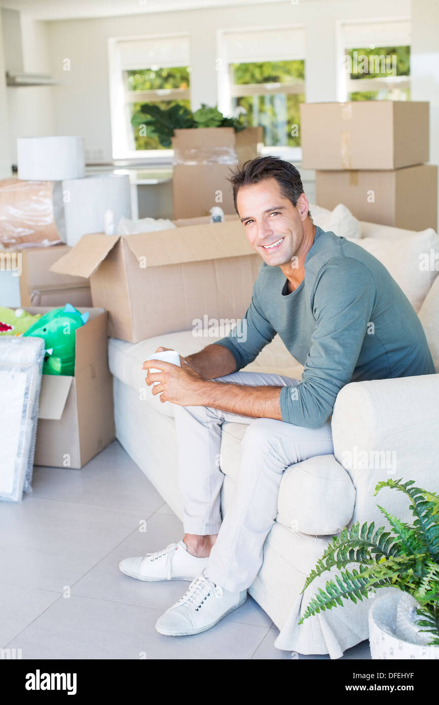 Porträt von lächelnder Mann Kaffeegenuss auf Sofa unter Kartons Stockfoto