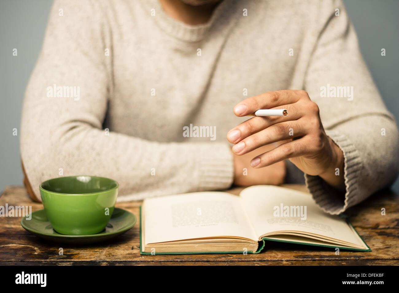 Mann lesen, Kaffee trinken und Rauchen eine Zigarette am Tisch Stockfoto