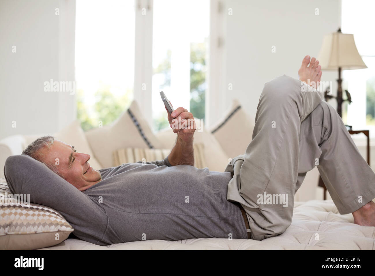 Ältere Mann mit Handy auf Bett Stockfoto