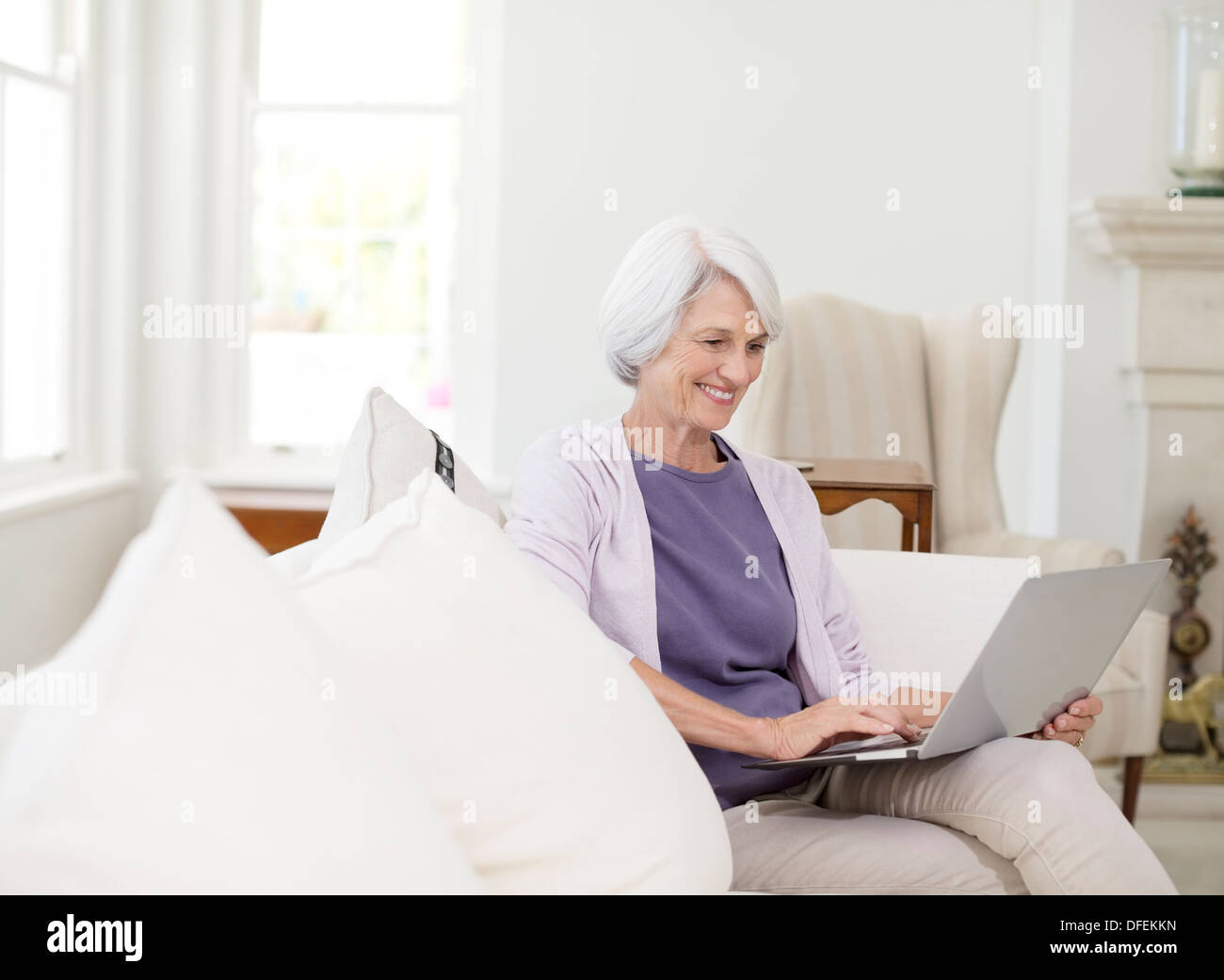 Ältere Frau mit Laptop auf dem Sofa im Wohnzimmer Stockfoto