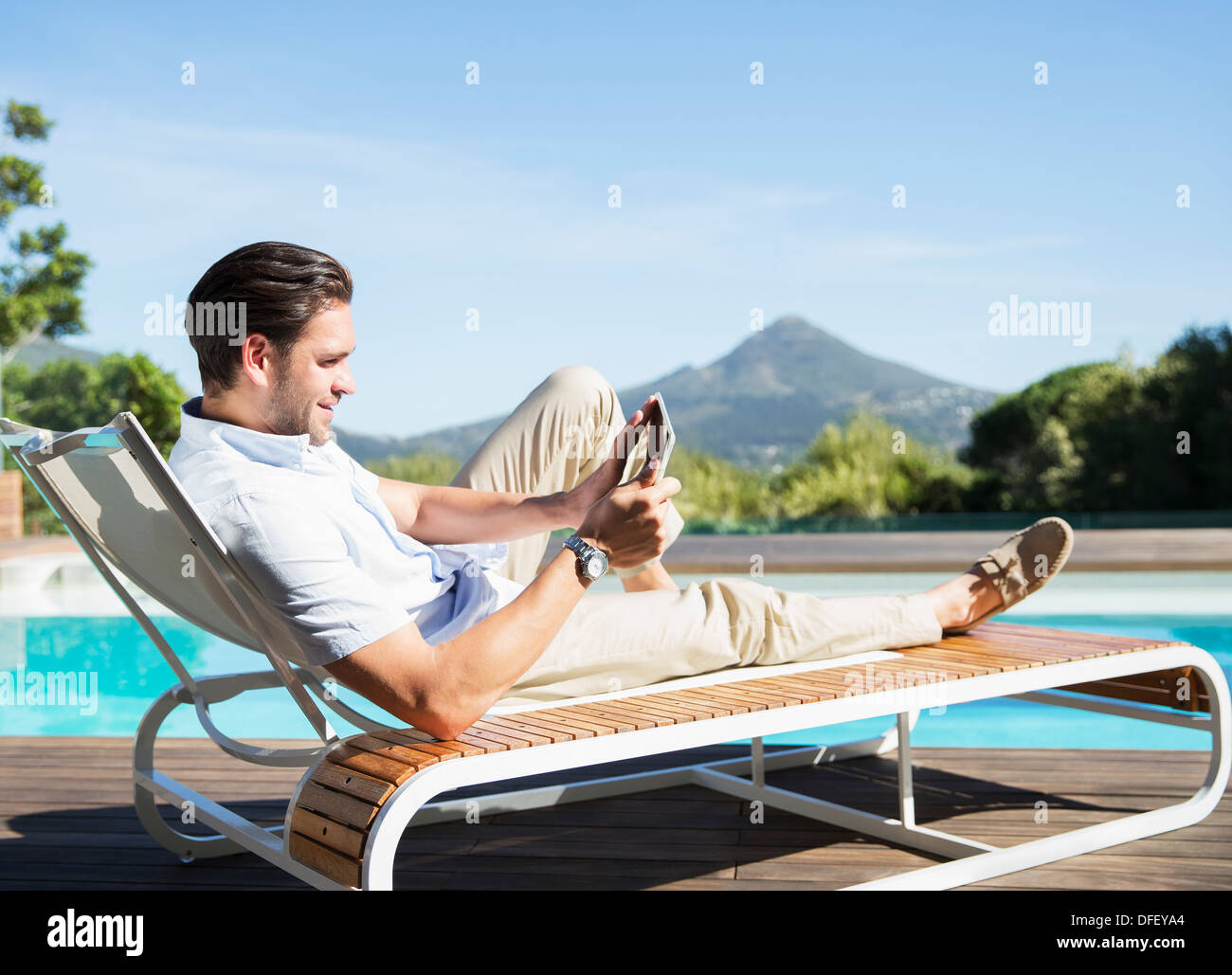 Mann Mit Digital Tablette Auf Liegestuhl Am Pool Stockfoto