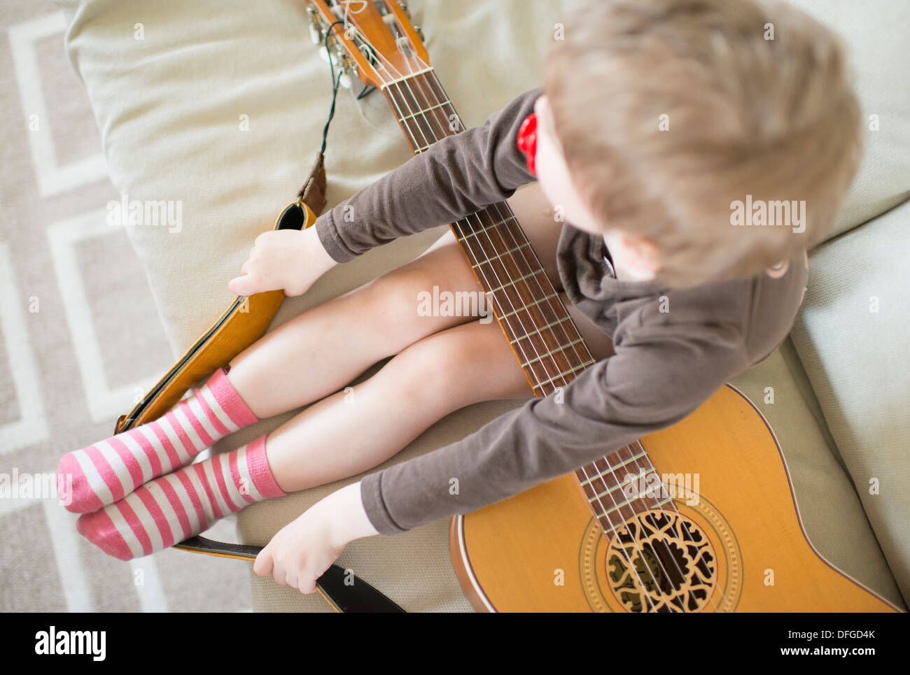 Junges Mädchen, 4 Jahre alt, sitzt im Sofa mit Akustik-Gitarre Stockfoto