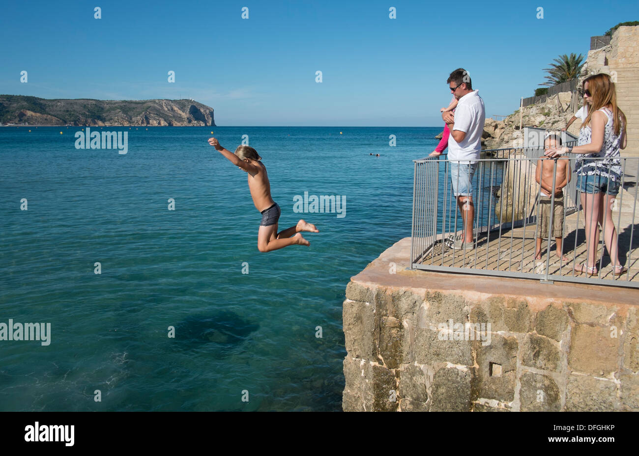 Ein kleiner Junge springt von einer hohen Mauer im Meer in Javea, Spanien. Stockfoto