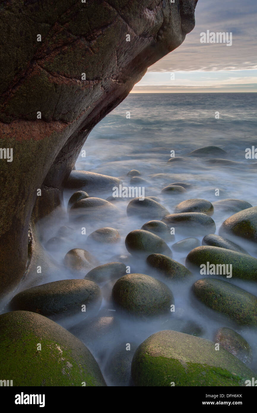 Wellen brechen über Felsblöcke unter einem Felsen Überhang Porth Nanven, Cornwall Stockfoto