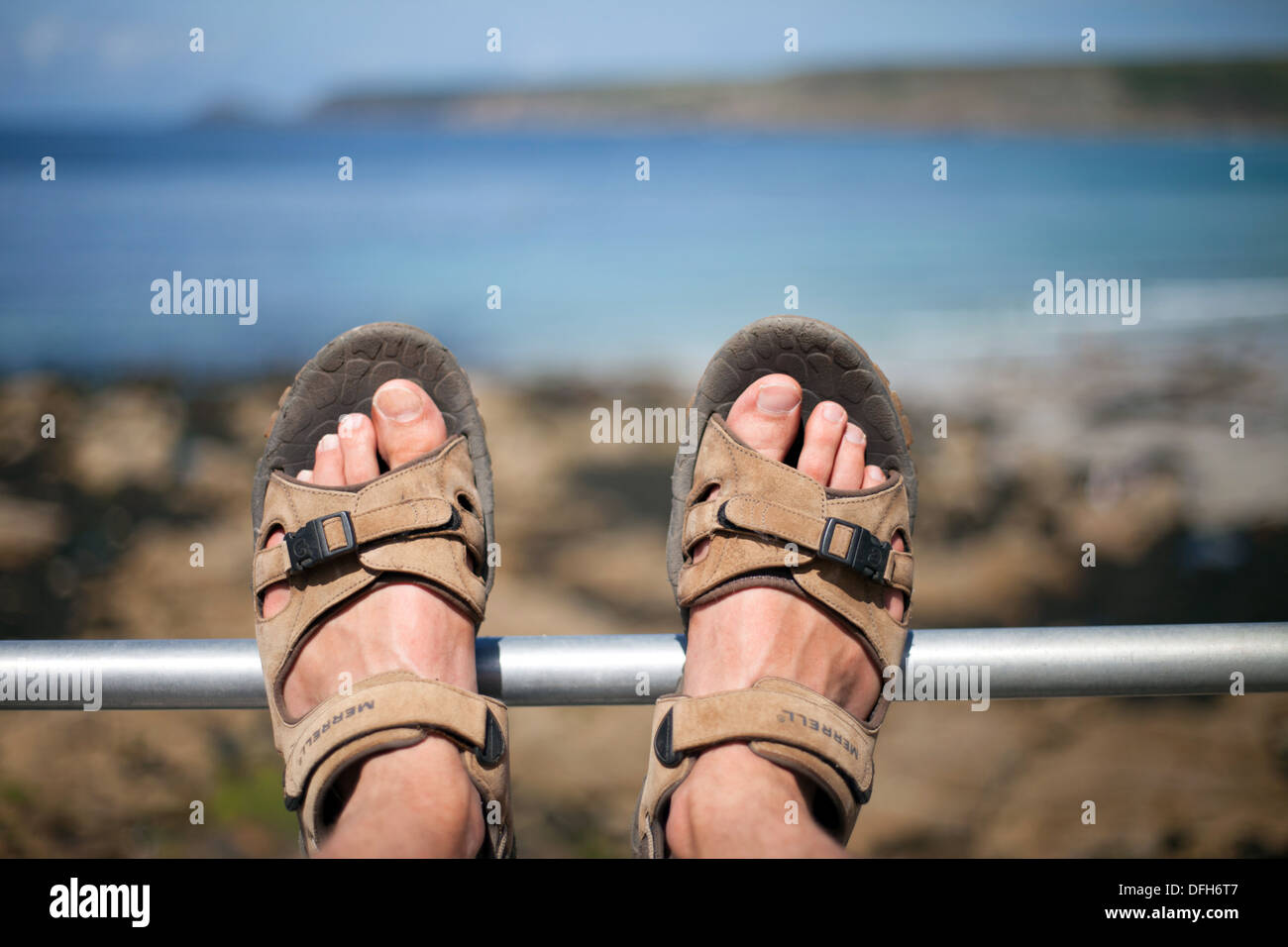 Füße tragen Sandalen auf dem Geländer Sennen Cove Cornwall, Sommerurlaub, UK Stockfoto