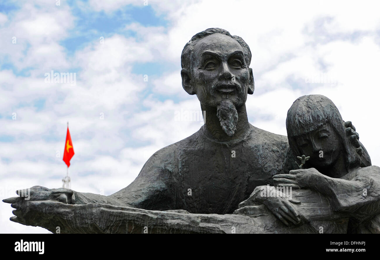 Statue von Ho Chl Minh und kleine Mädchen, die eine Blume mit der kommunistischen roten Flagge. Stockfoto