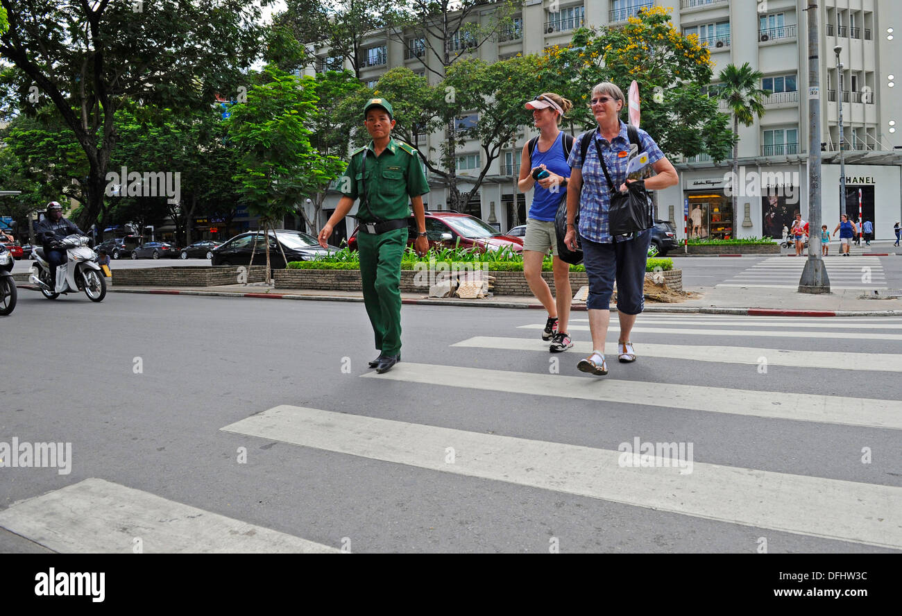 Vietnamesische Traffic Warden eskortieren Touristen über eine stark befahrene Straße in Ho-Chi-Minh-Stadt. Stockfoto