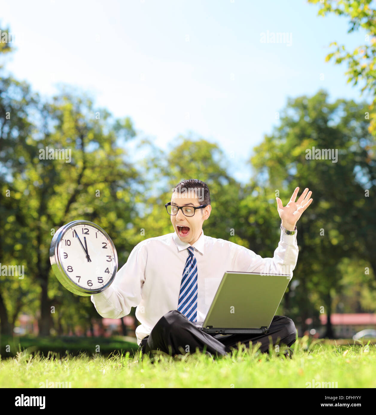 Junge wütend Unternehmer mit Laptop auf dem grünen Rasen sitzen und Blick auf die Uhr in einem park Stockfoto