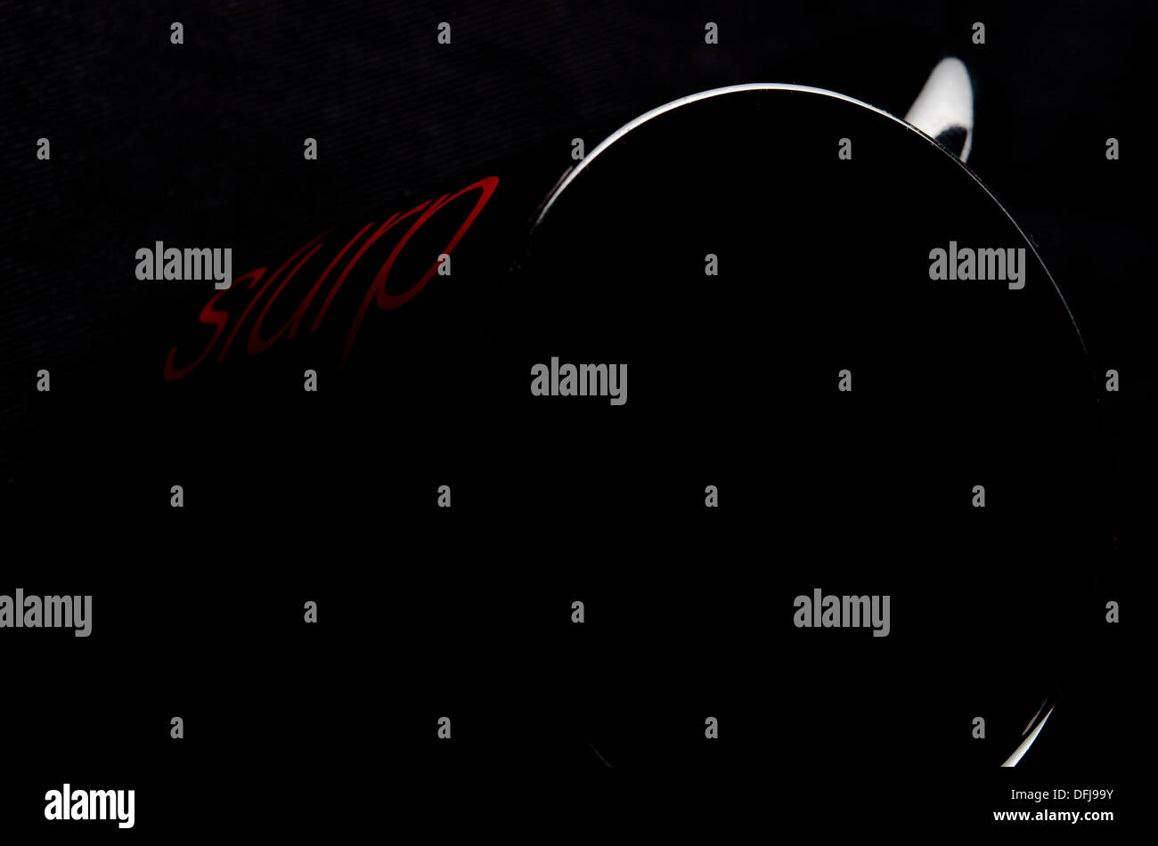 schwarzer Kaffeebecher mit roter Schrift auf schwarzem Hintergrund erschossen Stockfoto