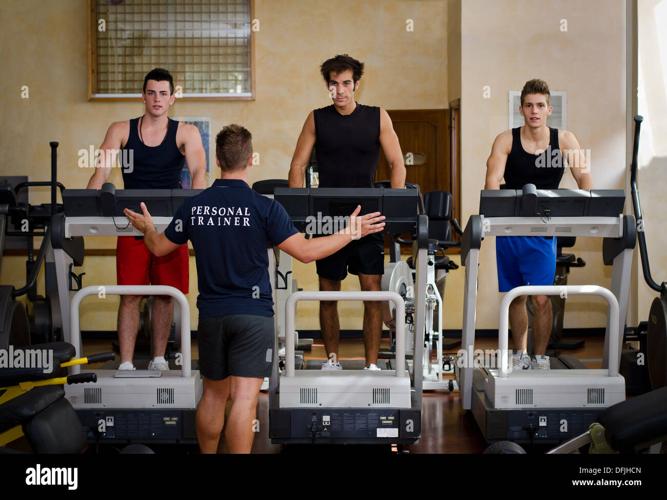 Drei junge Männer auf Laufbändern mit personal Trainer in einem Fitnessstudio trainieren. Stockfoto