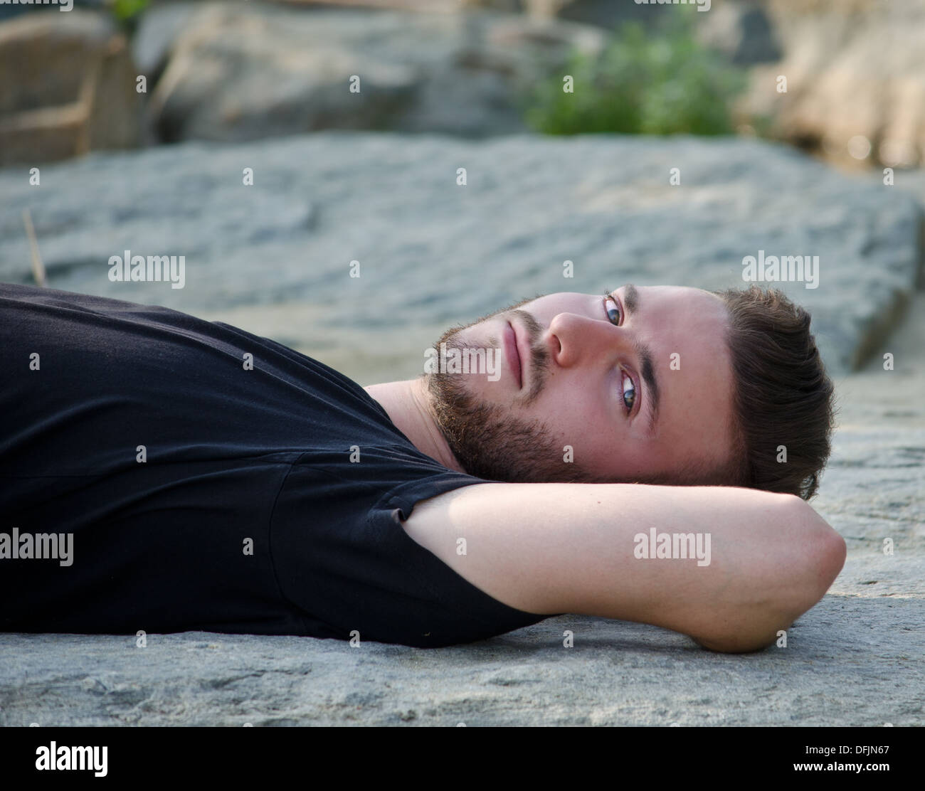 Hübscher junger Mann auf dem Rücken auf einem Felsen liegend auf der Suche unter Ausschluss der Öffentlichkeit, im freien Stockfoto