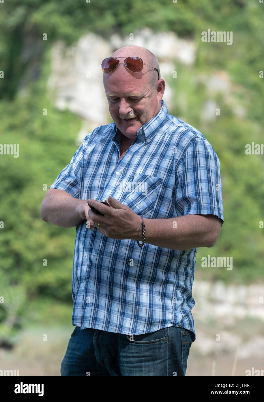 MANN, DIE SMS AUF HANDY/MOBILE TELEFON IM FREIEN UK Stockfoto