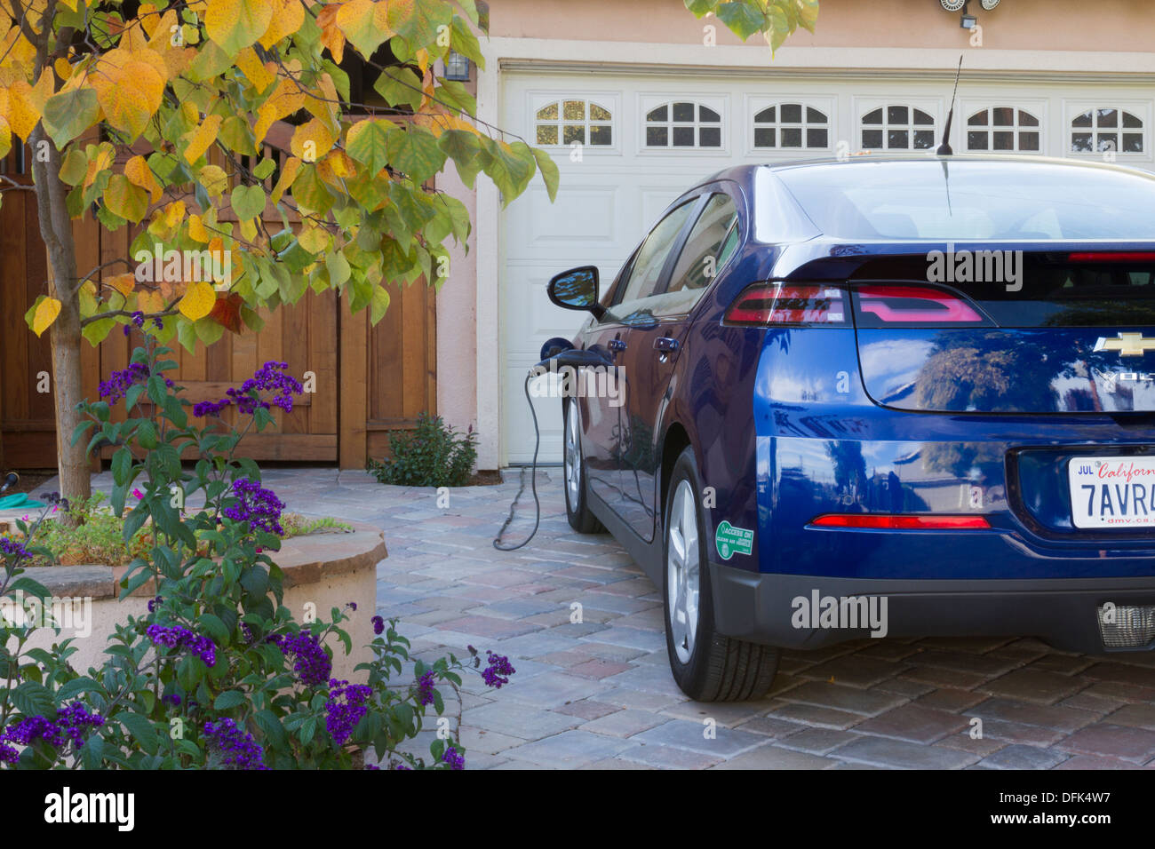 Plug-in-Elektro-Auto mit Fahrgemeinschaft Aufkleber in Einfahrt, mit Stecker eingesteckt und aufladen zu Hause geparkt Stockfoto