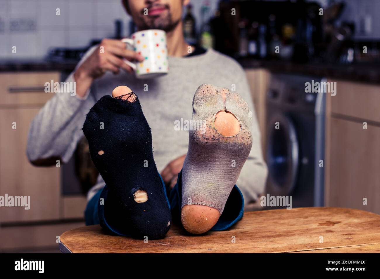 Junger Mann mit getragenen Socken am Tisch Stockfoto
