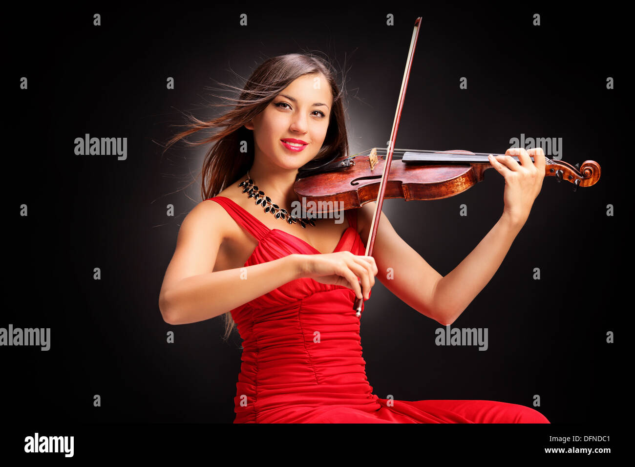 Junge attraktive Frau im roten Kleid mit dem Geigenspiel Stockfoto