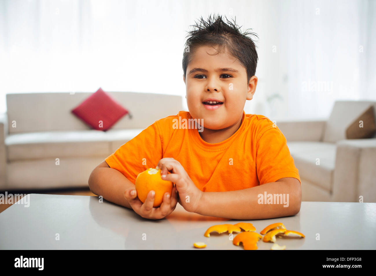 Junge sitzt an einem Tisch schälen einer orange Stockfoto