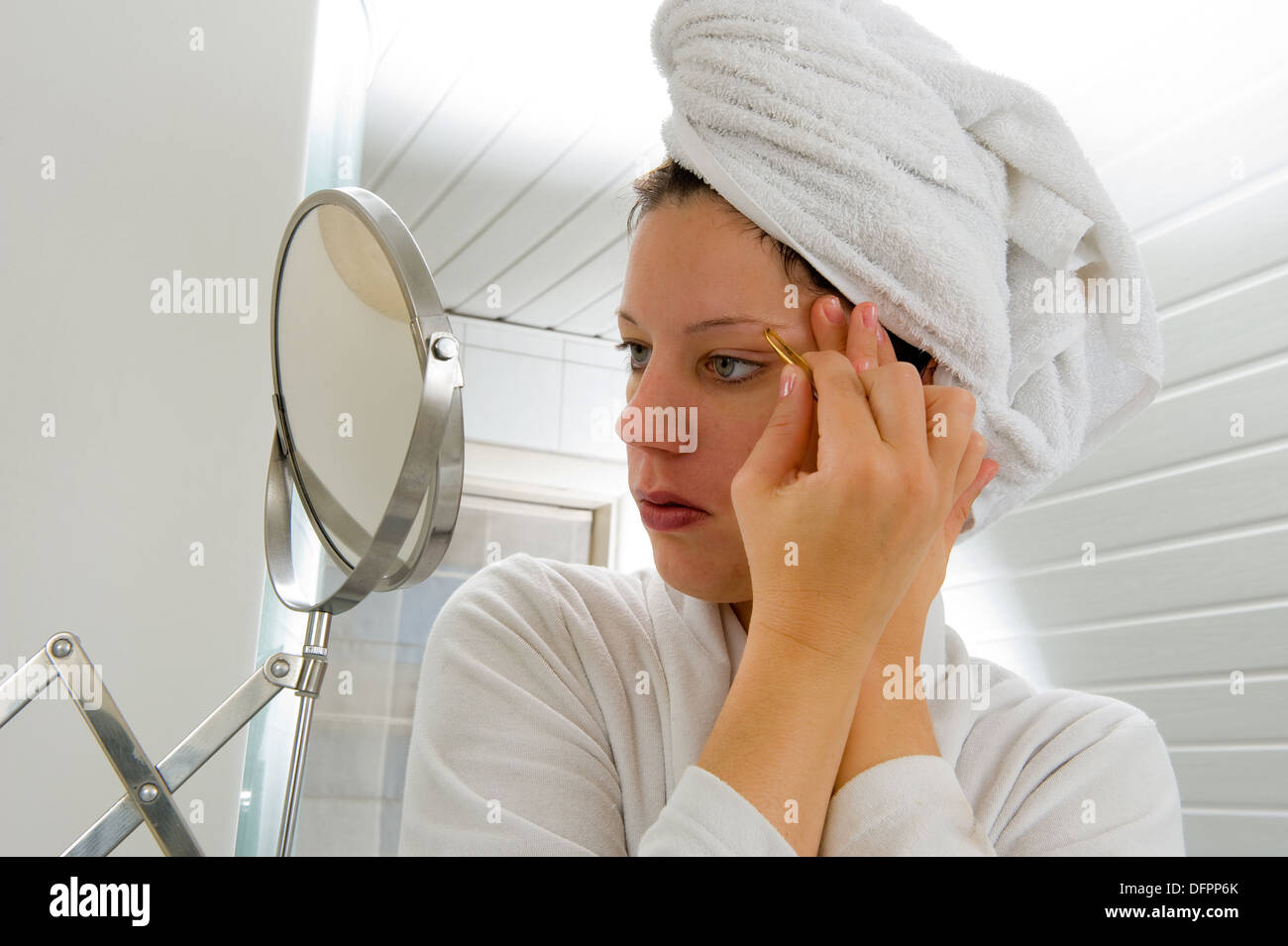Eine Frau sucht in den Spiegel, während sie ihre Augenbraue enthaaren ist Stockfoto