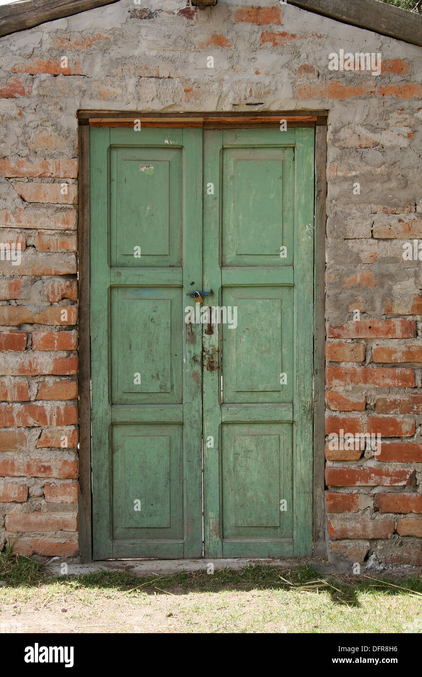 Eine grüne Holztür in einer Mauer aus Lehmziegeln in einem Gebäude in Cotacachi, Ecuador Stockfoto
