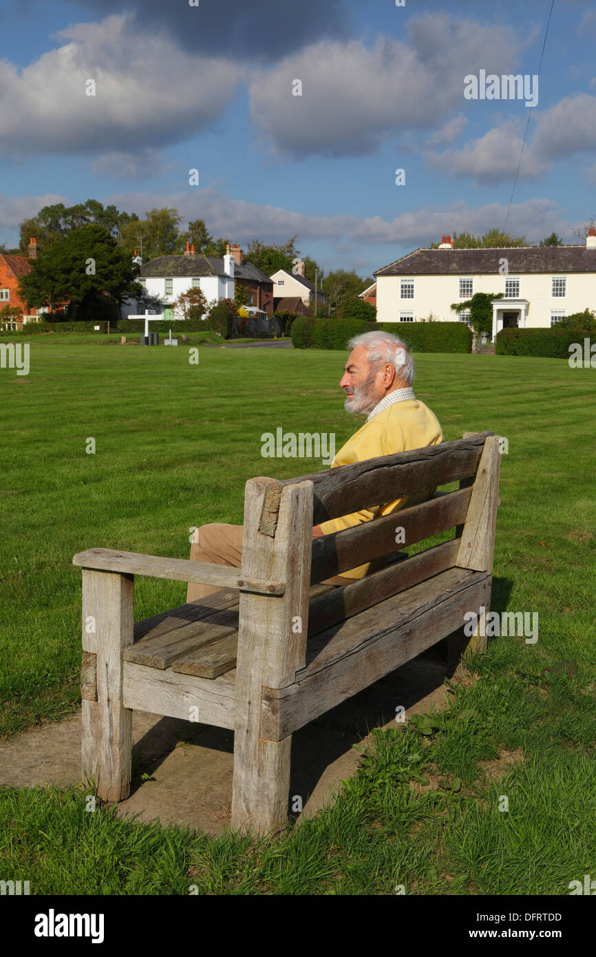 Älterer Mann sitzt auf einer Bank am Rushlake Green East Sussex England UK Stockfoto