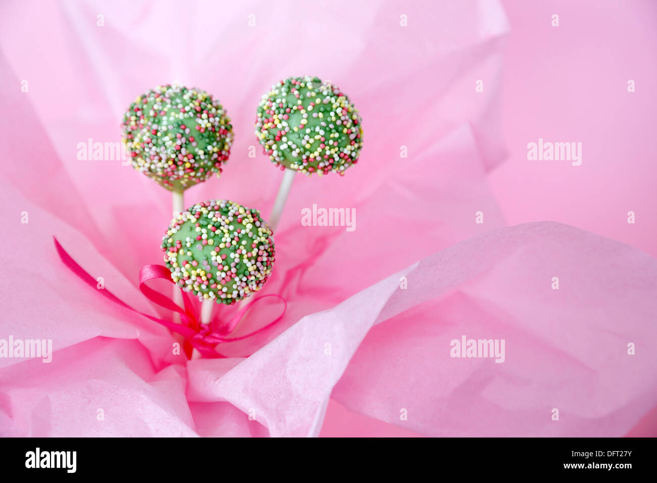 Cake Pop in grüne Schokolade getaucht und mit Streuseln verziert. In rosa Seidenpapier gewickelt. Stockfoto