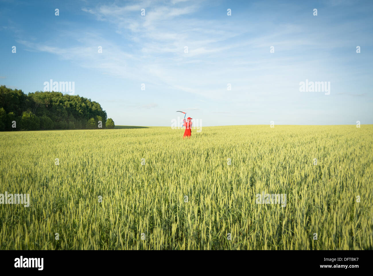 Person trägt rote Haube und Sense im grünen Bereich Stockfoto