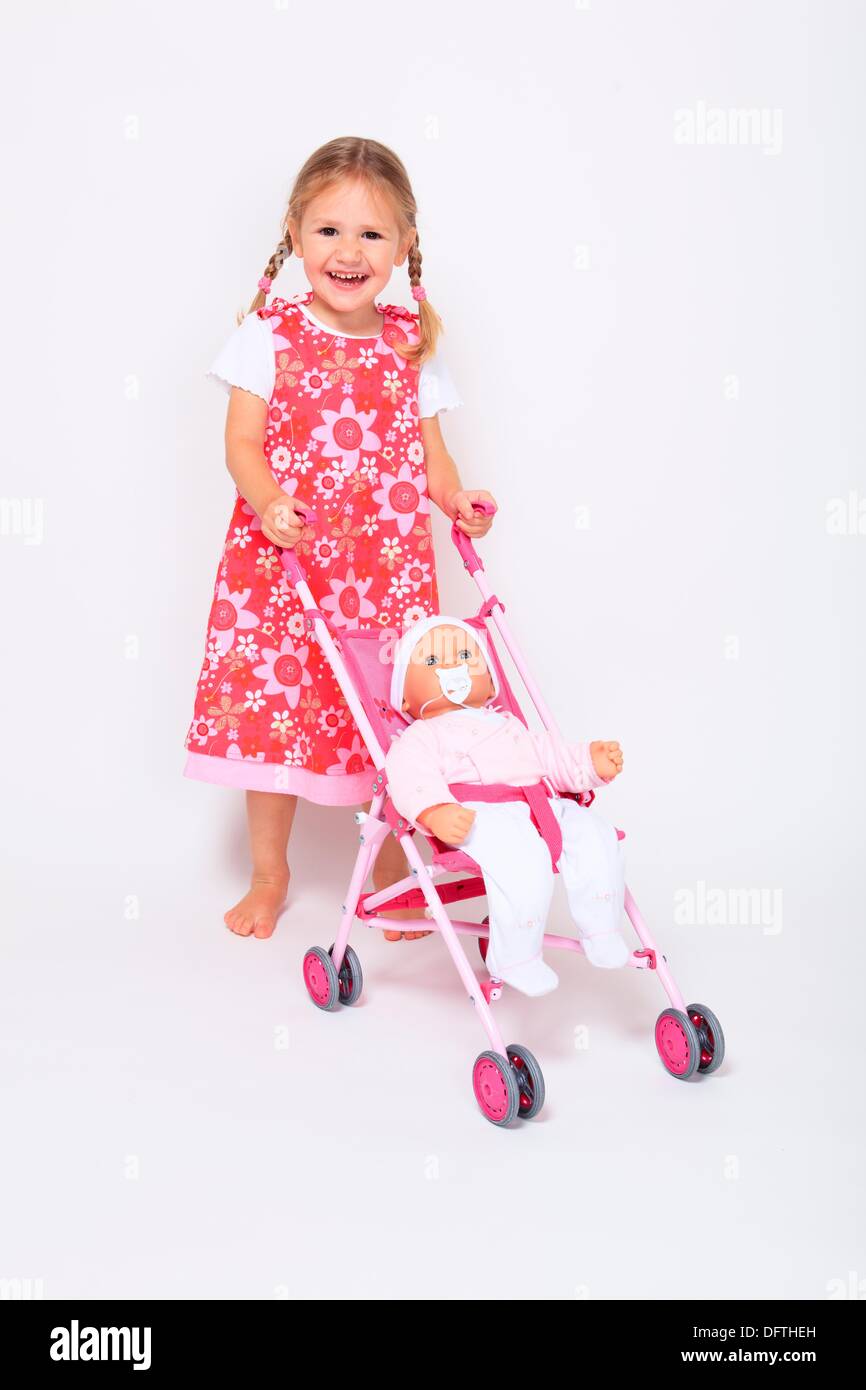 kleine Mädchen tragen Kleid stehend mit Buggy Kinderwagen und Baby-Puppe,  weißer Hintergrund, Studio, Schweiz Stockfotografie - Alamy