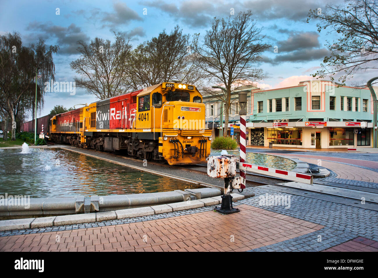 Eine lange Kiwi Rail Güterzug führt über einen Bahnübergang, der durch die Mitte der Art deco Stadt Hastings, North Island, Neuseeland Stockfoto