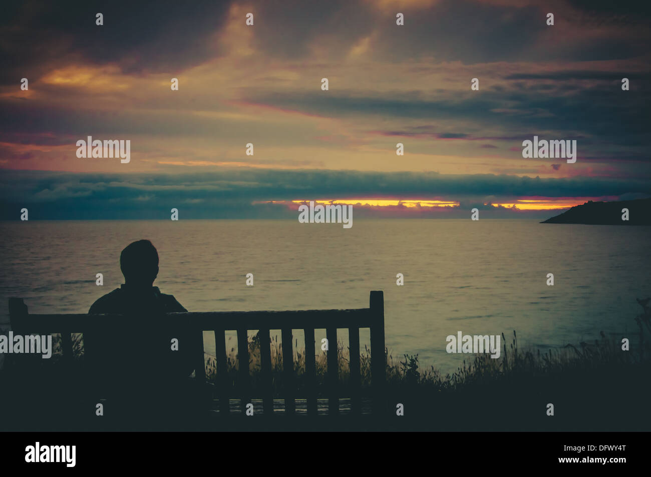 Ein Mann saß auf einer Bank, Blick auf den Sonnenuntergang über dem Meer Stockfoto
