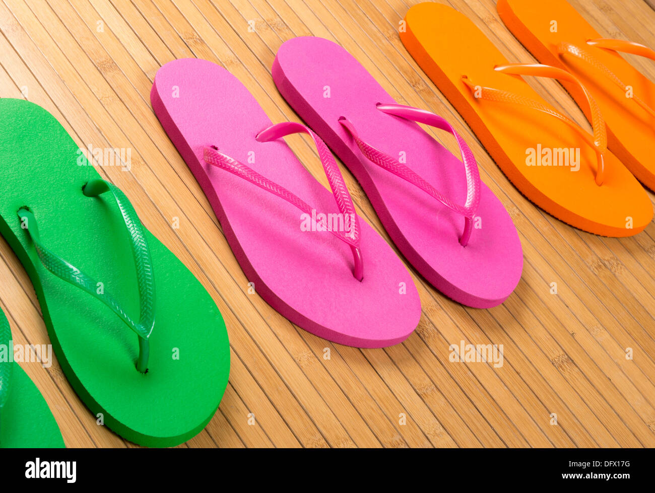 Grün, Flip-Flop Pink und Orange Sandalen auf Bambusmatte in Nahaufnahme Stockfoto